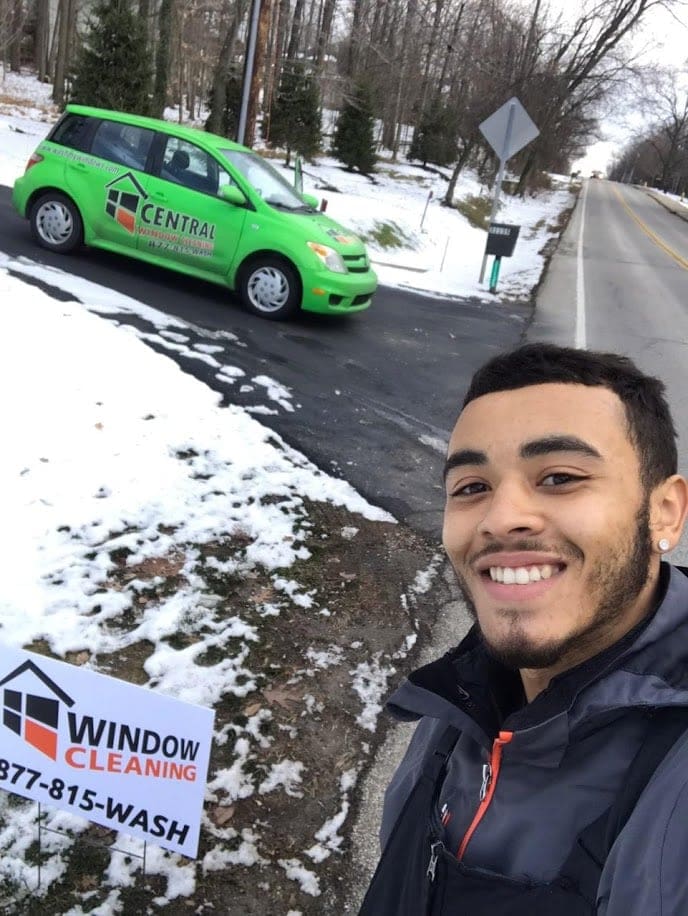 Smiling technician taking a selfie next to a company sign, with a green Central Window Cleaning van parked on a snowy roadside.