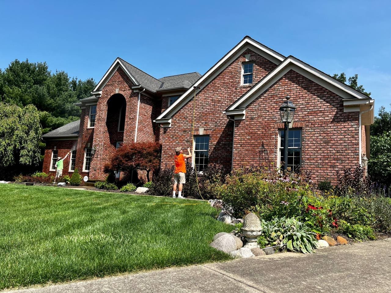 Two Central Window Cleaning technicians washing windows on a brick residential home, Akron OH area